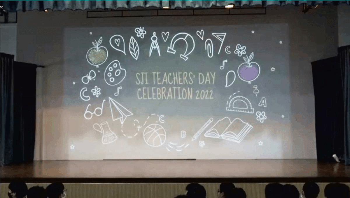 Stage screen displays "SJI Teachers' Day Celebration 2022" surrounded by school-themed doodles, with audience seated below.