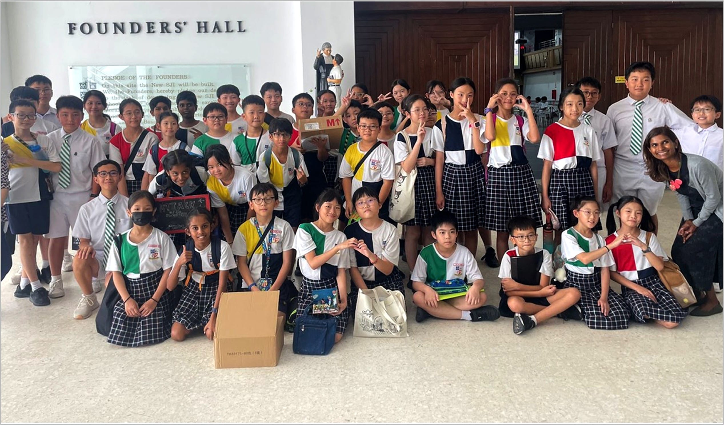 A large group of uniformed school students posing together inside Founders' Hall.