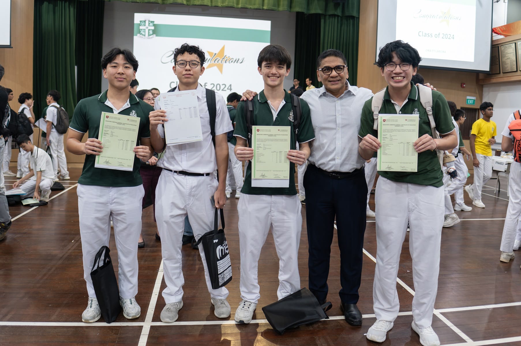 Five people pose in a school hall holding certificates, with a Class of 2024 congratulations banner behind them.