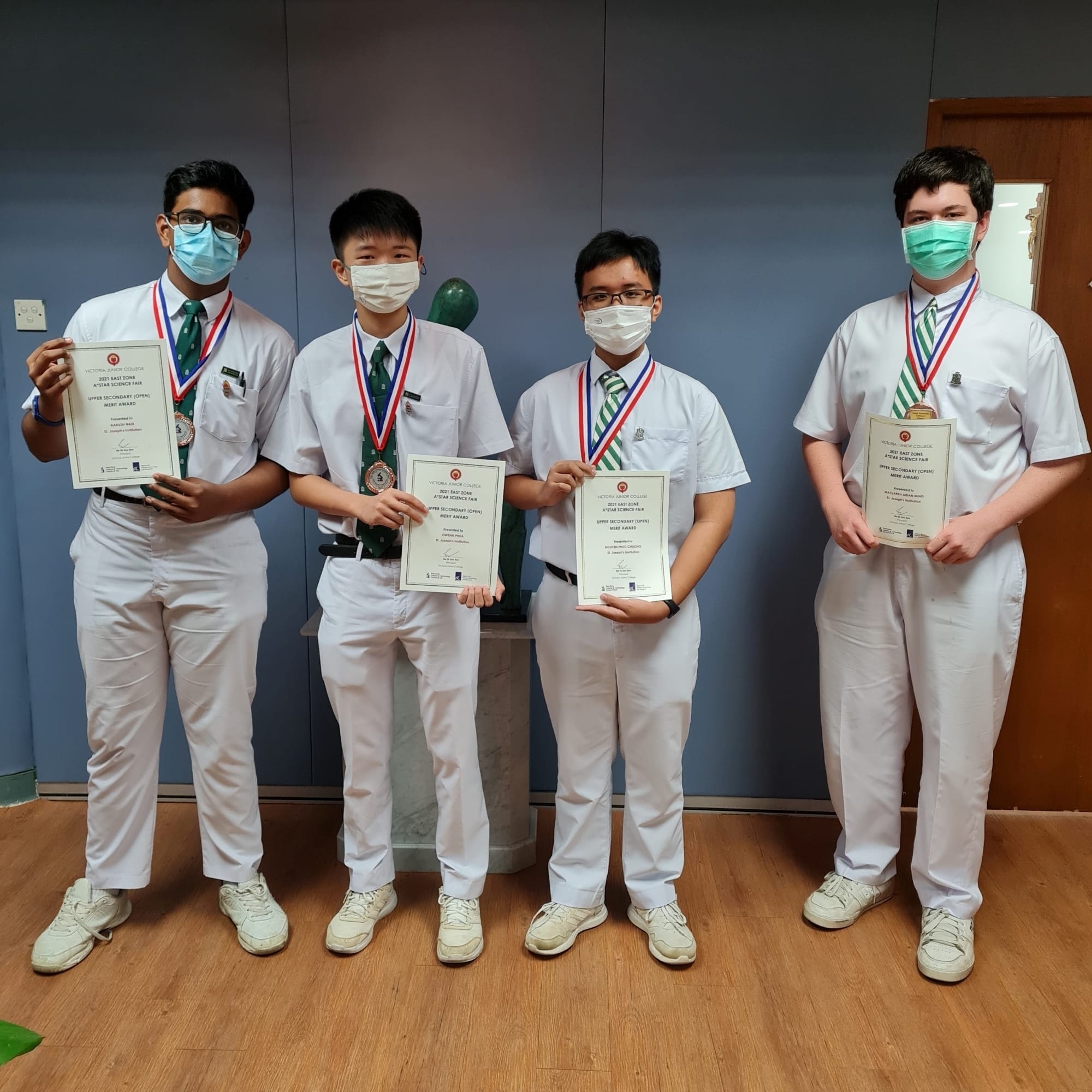 Four students wearing medals hold their 2021 East Zone A*STAR Science Fair Upper Secondary Merit Award certificates.