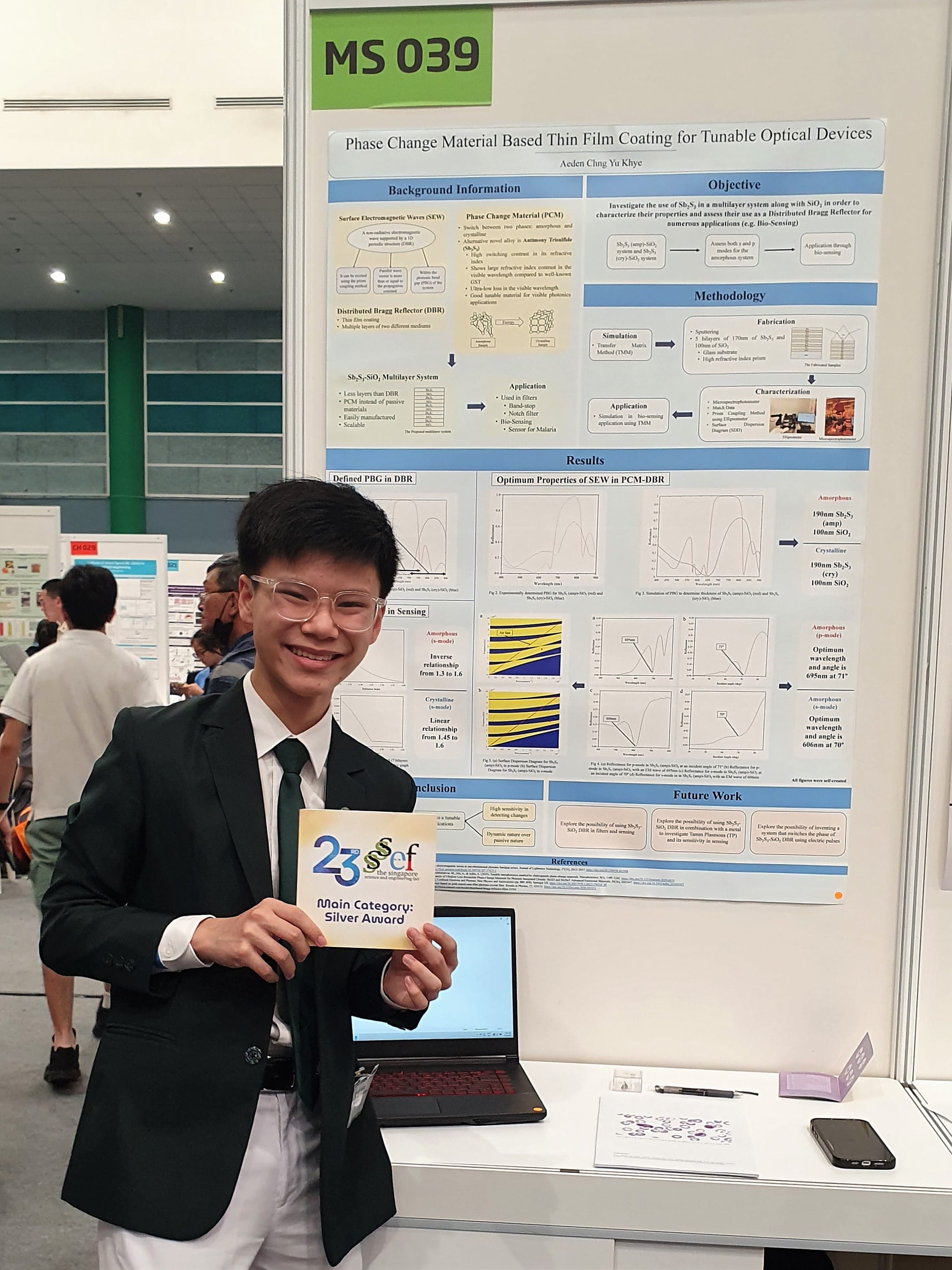 A student holds a Silver Award card beside his SSEF poster 'Phase Change Material Based Thin Film Coating for Tunable Optical Devices', board MS 039.