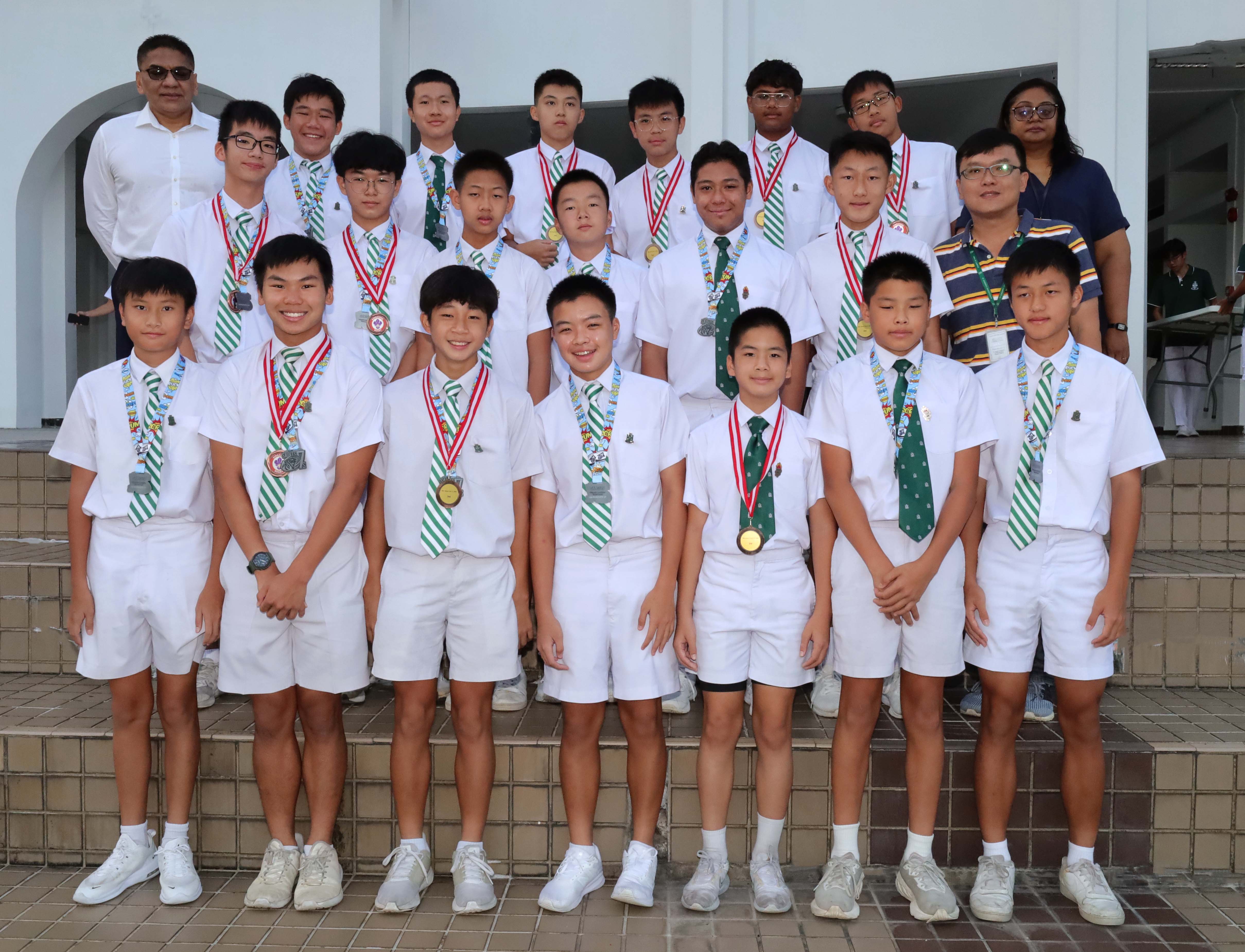 A group of young male students in white uniforms and green striped ties wearing medals, posing with two adult supervisors.