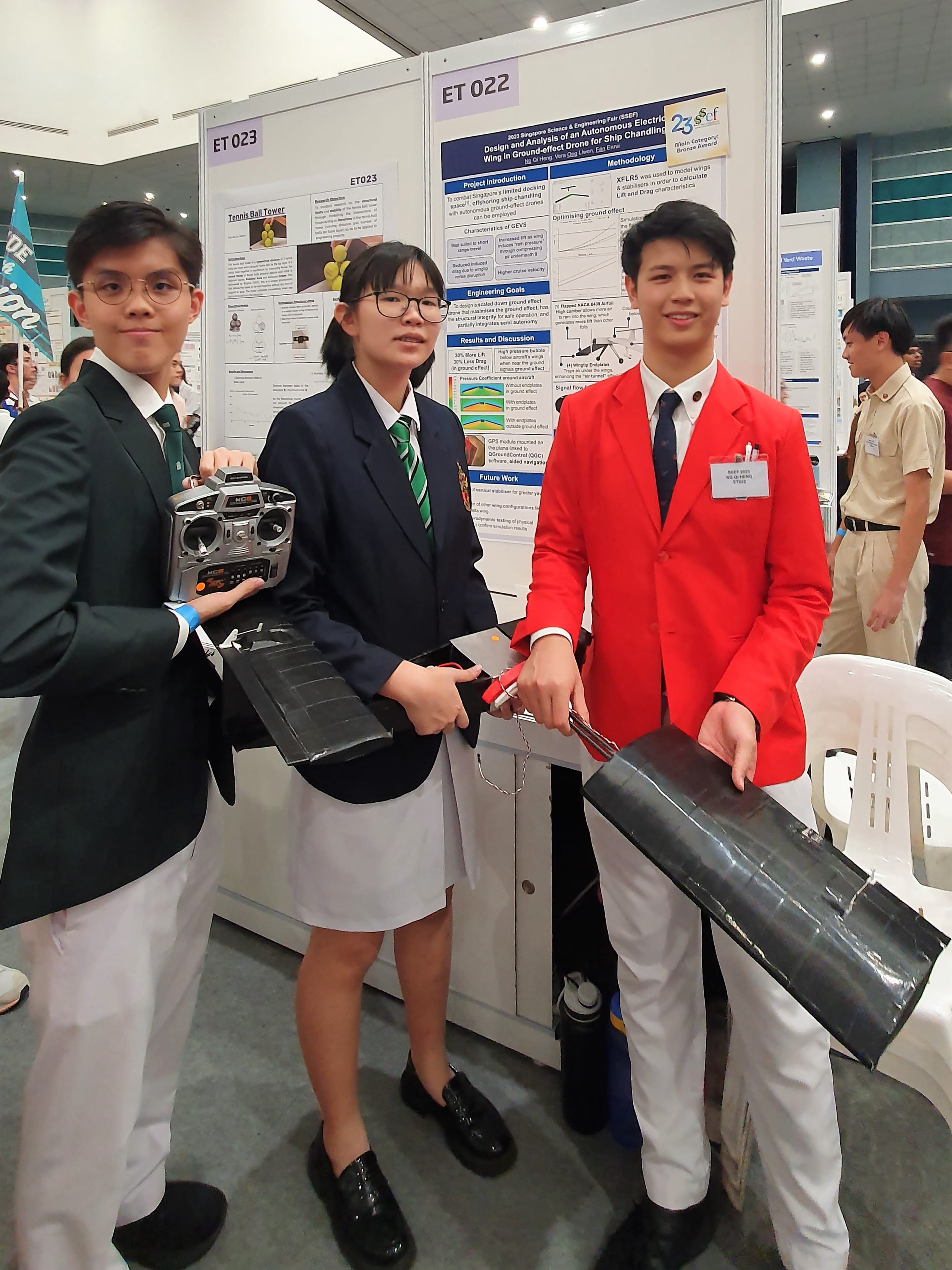 Three students hold model wings and a controller beside their SSEF poster on an autonomous drone wing for ship chandling, board ET 022.