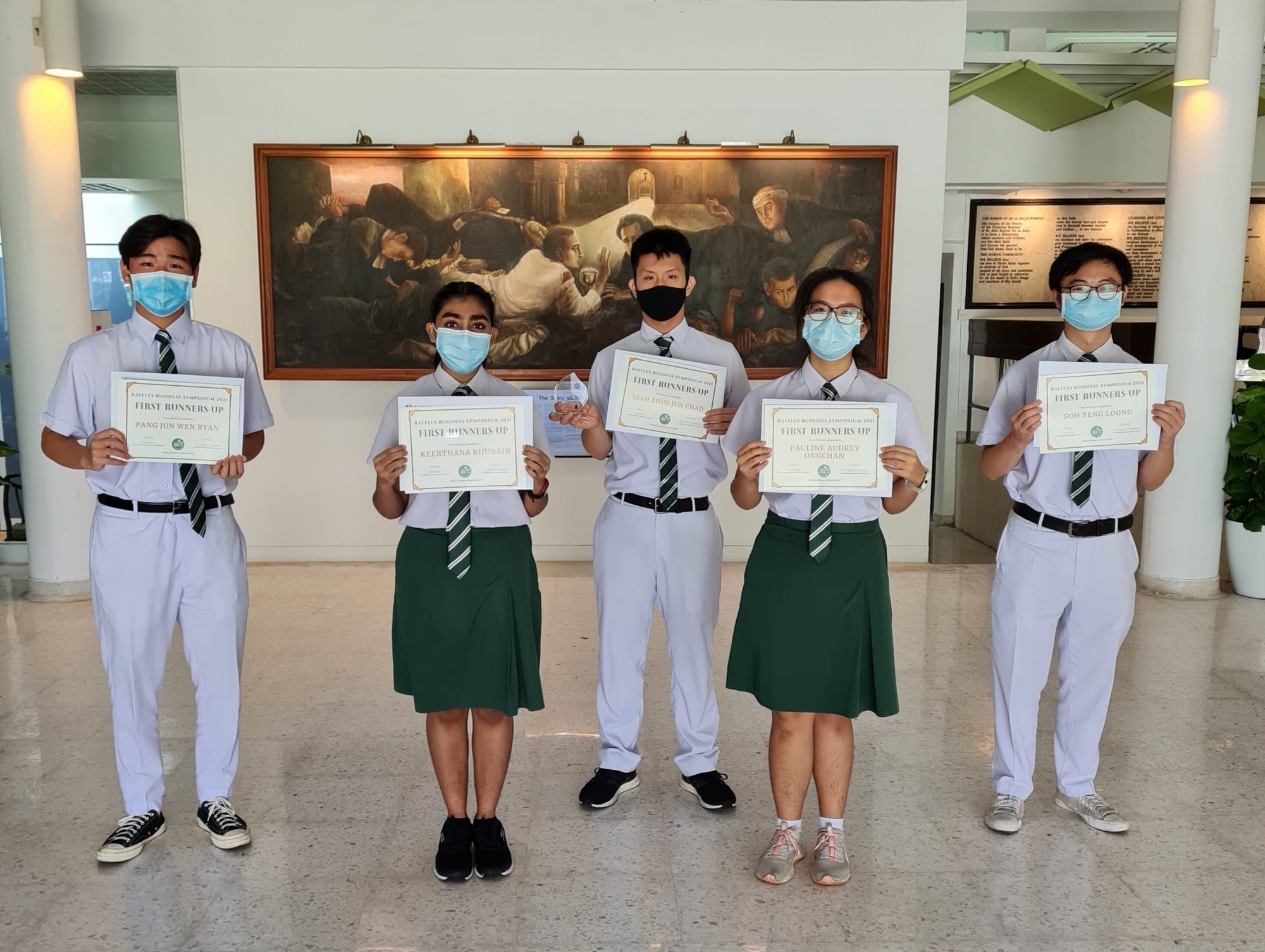 Five masked students in school uniforms hold First Runners-Up certificates indoors in front of a large painting.