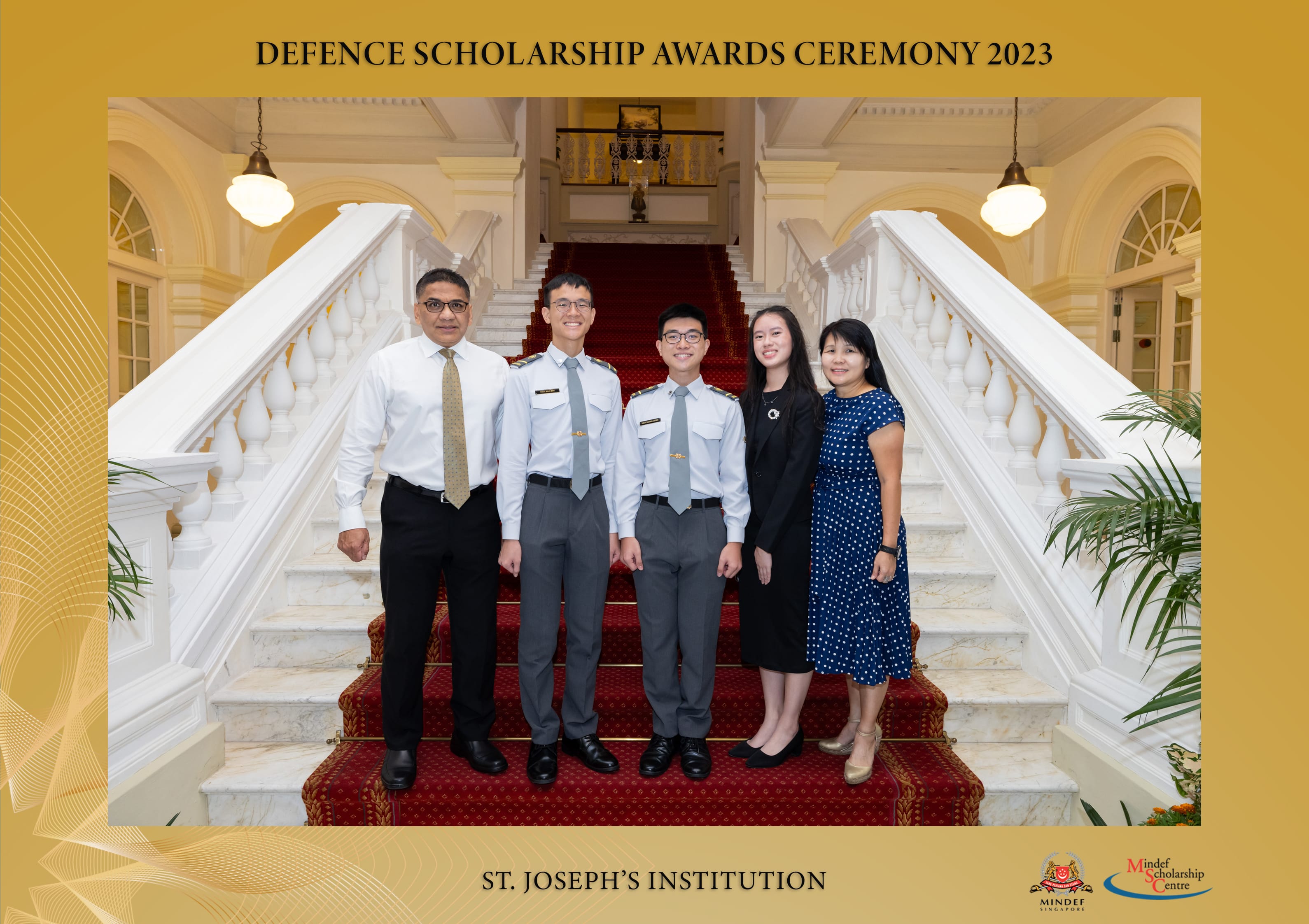 Five people, including two uniformed scholars, pose on a grand staircase at the Defence Scholarship Awards Ceremony 2023, St. Joseph's Institution.