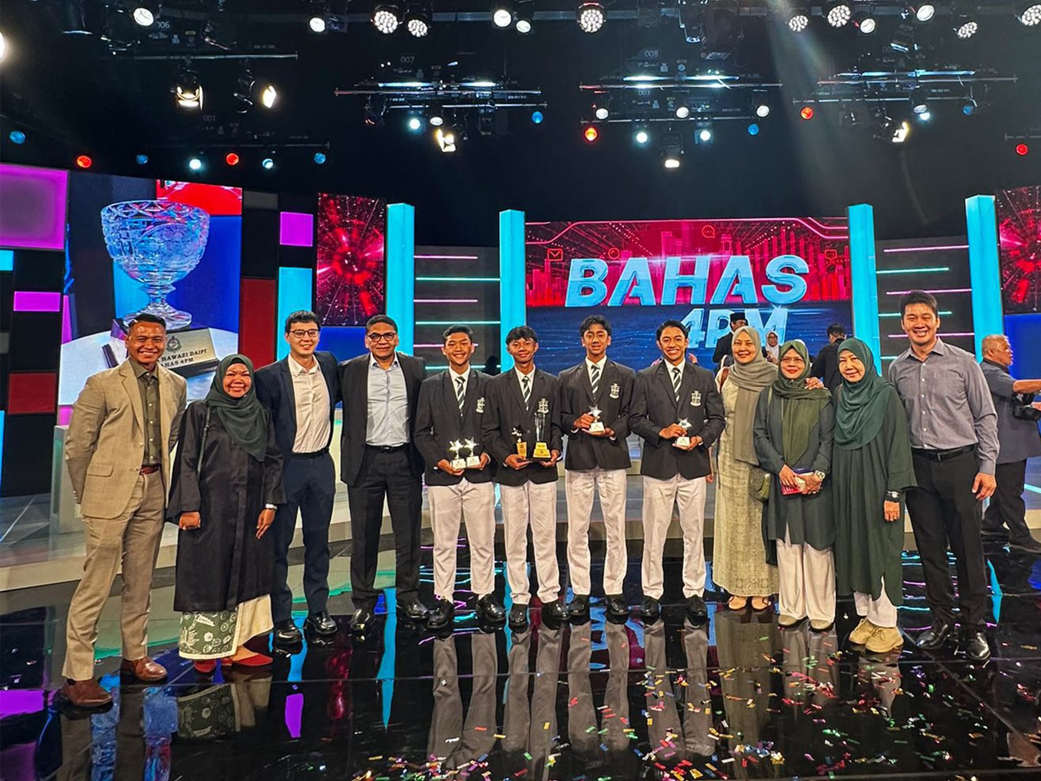 Group of people posing on a TV studio stage with trophies in front of a "BAHAS 4PM" backdrop.
