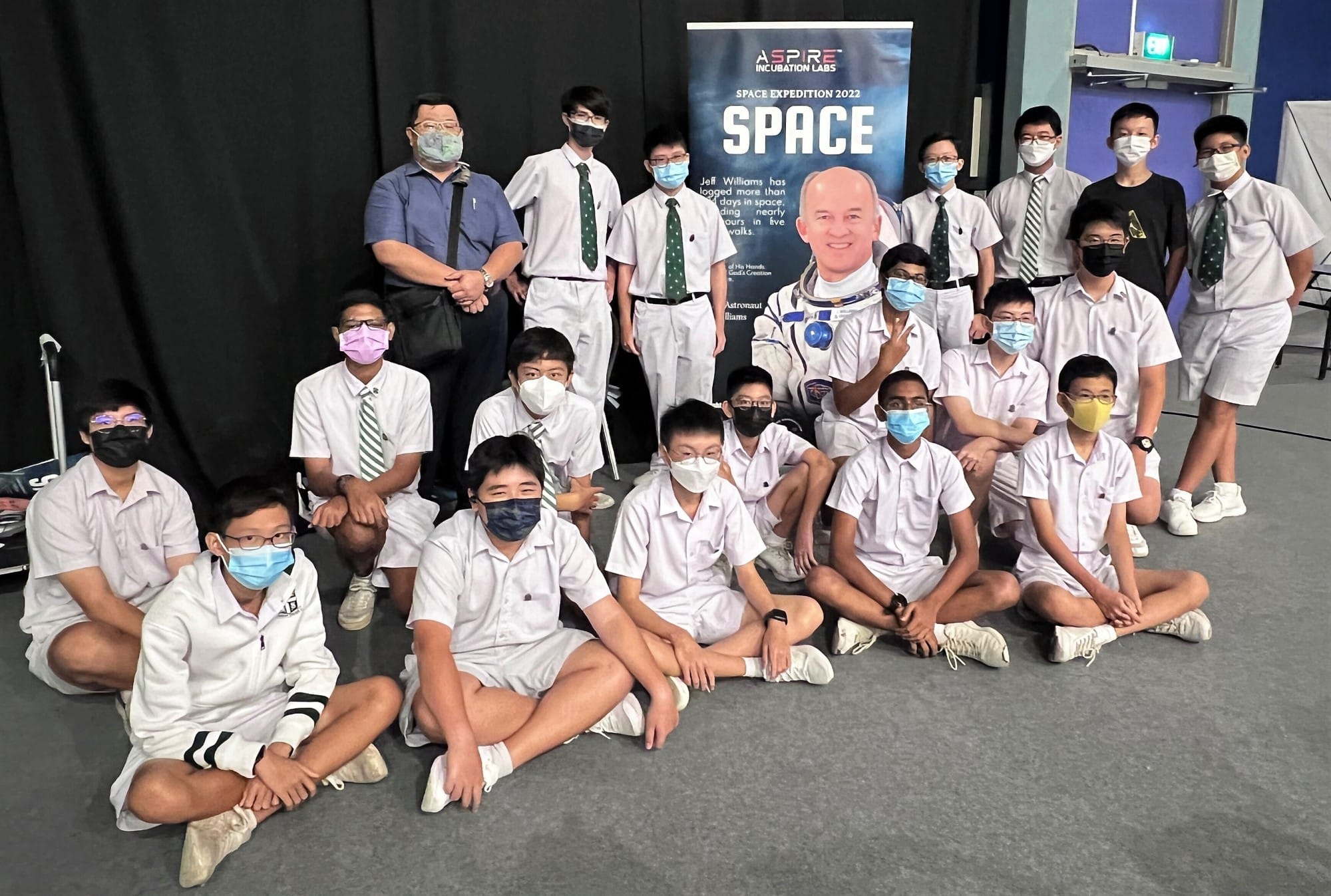 Group of masked students in white uniforms pose near an Aspire Incubation Labs Space Expedition 2022 banner.