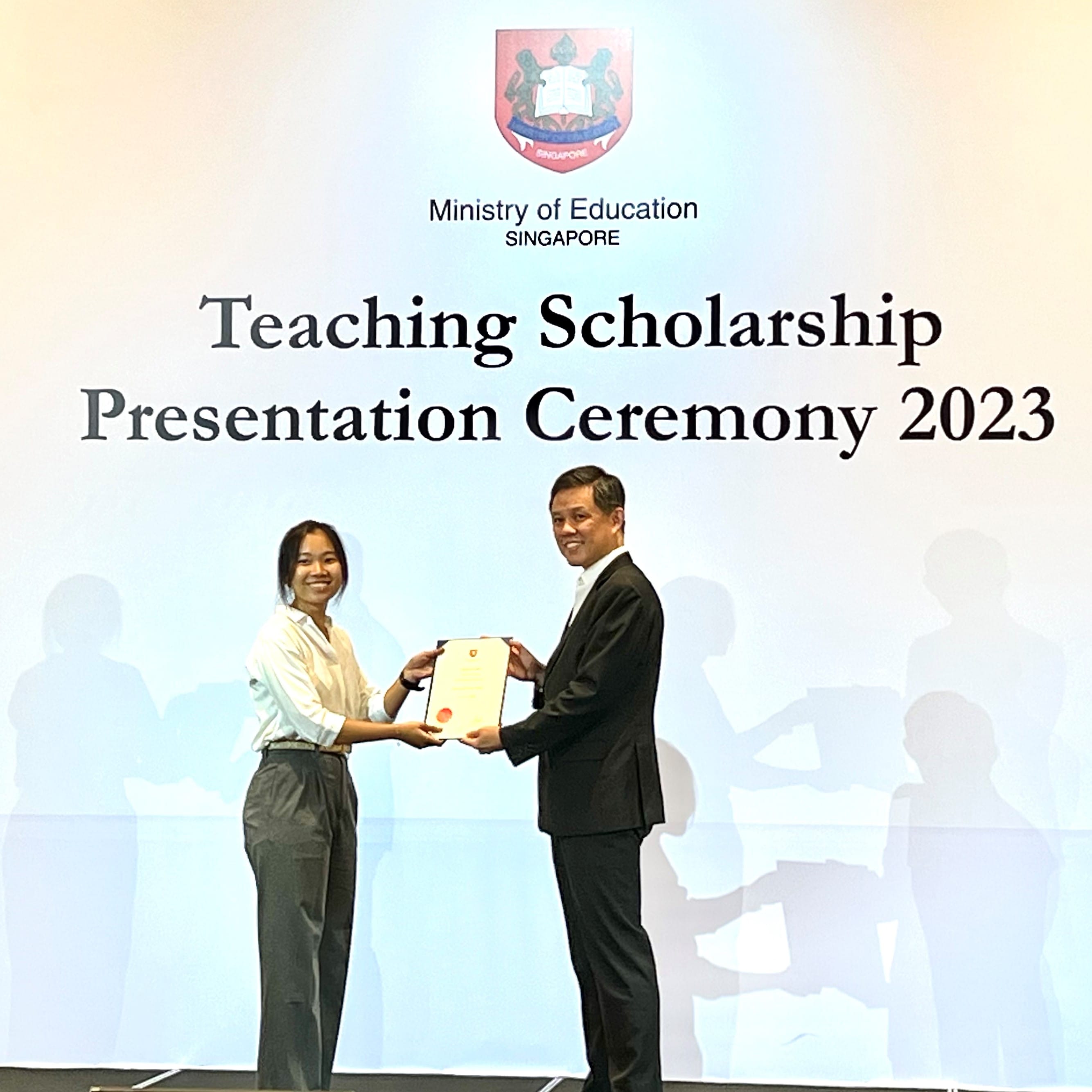 A woman receives a certificate from a man on stage at the MOE Teaching Scholarship Presentation Ceremony 2023.