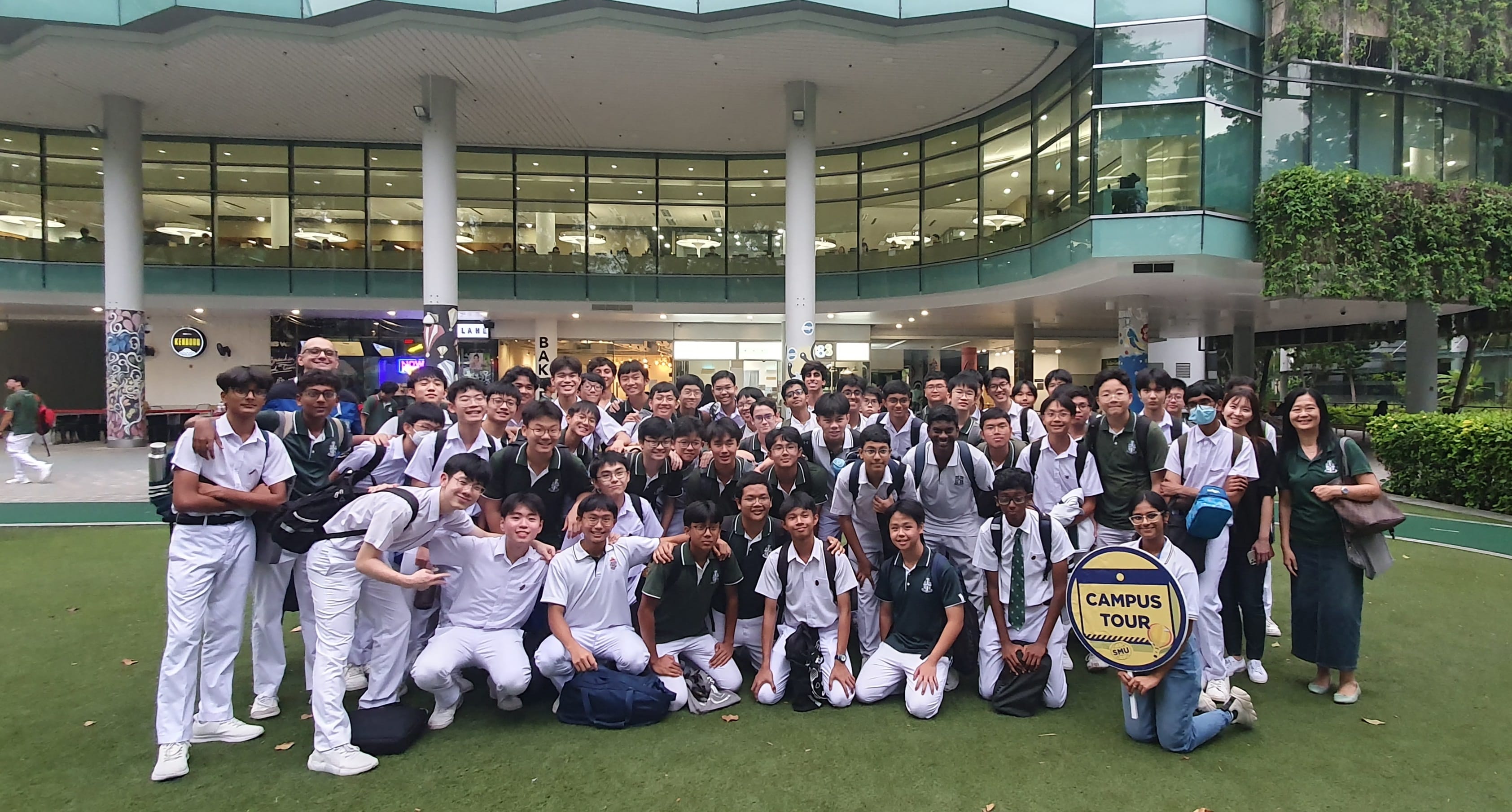 Large group of students in white uniforms posing outdoors at an SMU Campus Tour in front of a modern building.