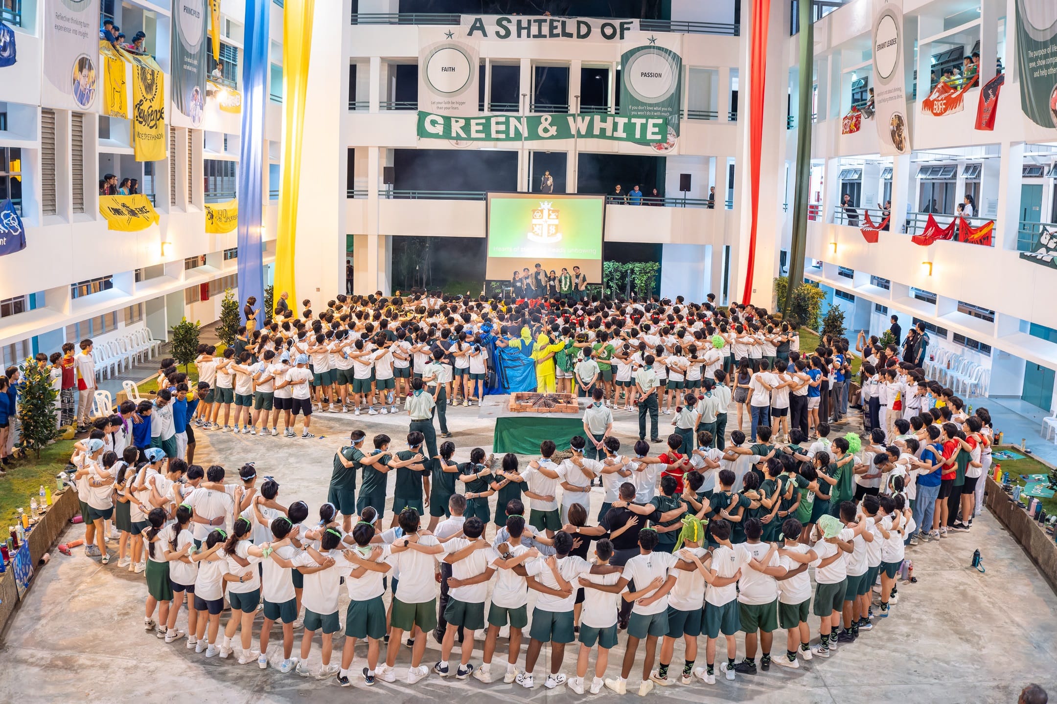 Students in green and white uniforms form a large circle in a school courtyard under a "Green & White" banner.