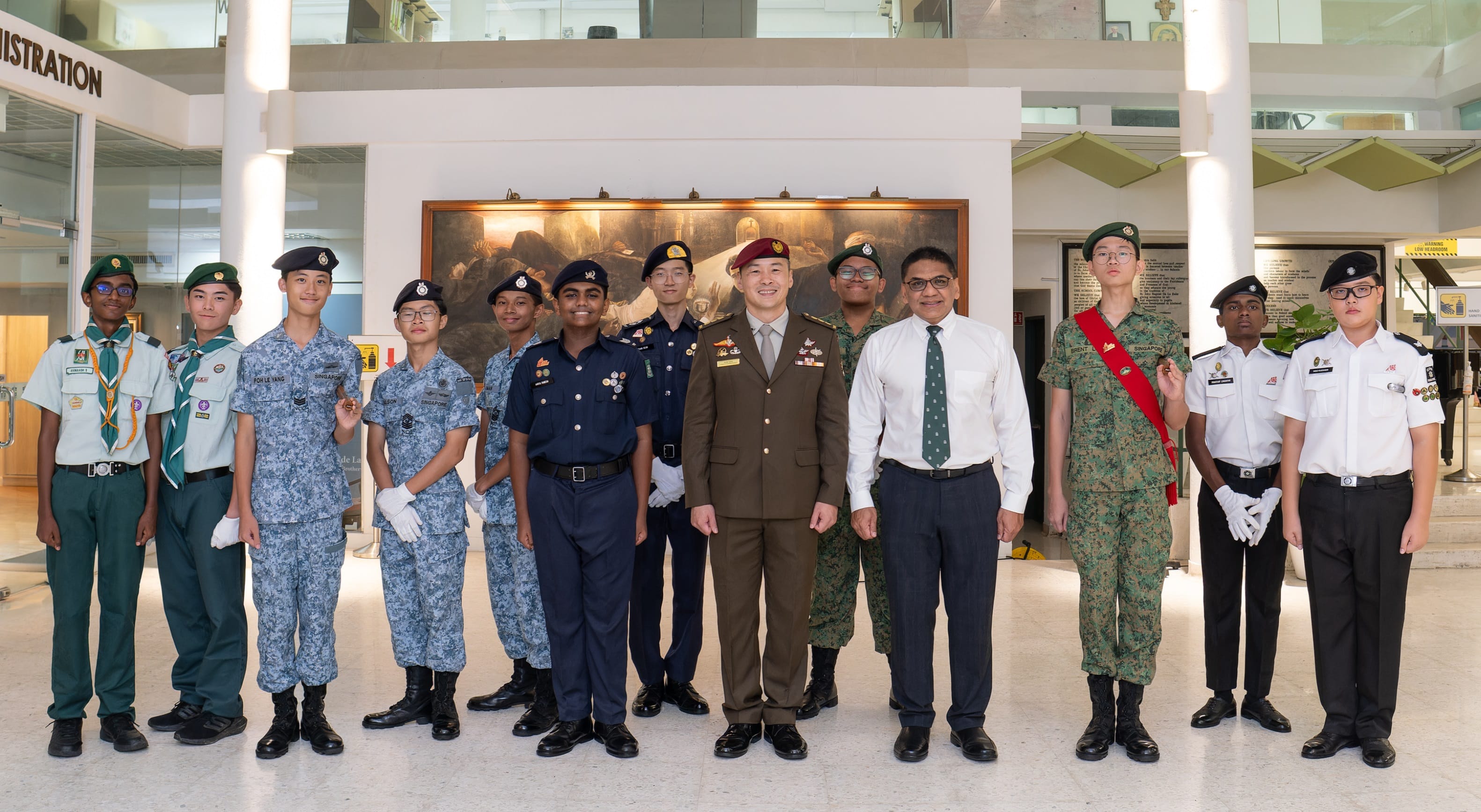 A group of youth and adults in various military and scout uniforms posing together indoors near a registration area.
