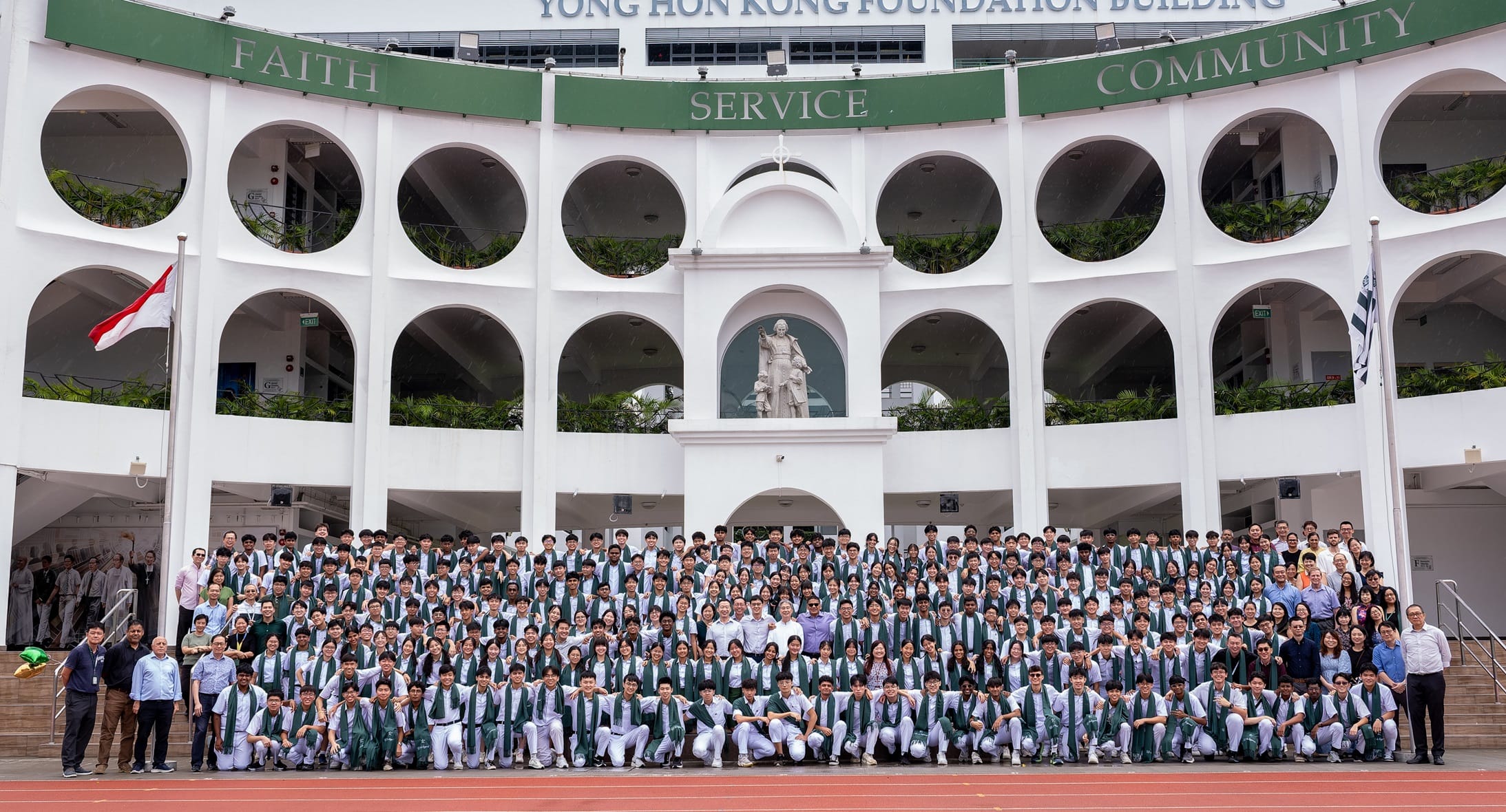 Large group of students in white uniforms with green sashes posing in front of the Yong Hon Kong Foundation Building.