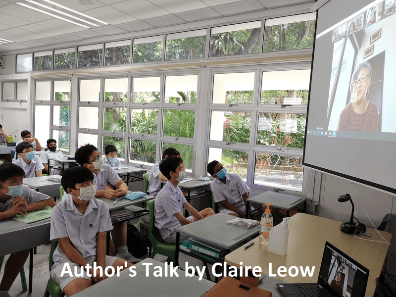 Students in school uniforms and masks watch author Claire Leow speak via video call projected on a classroom screen.