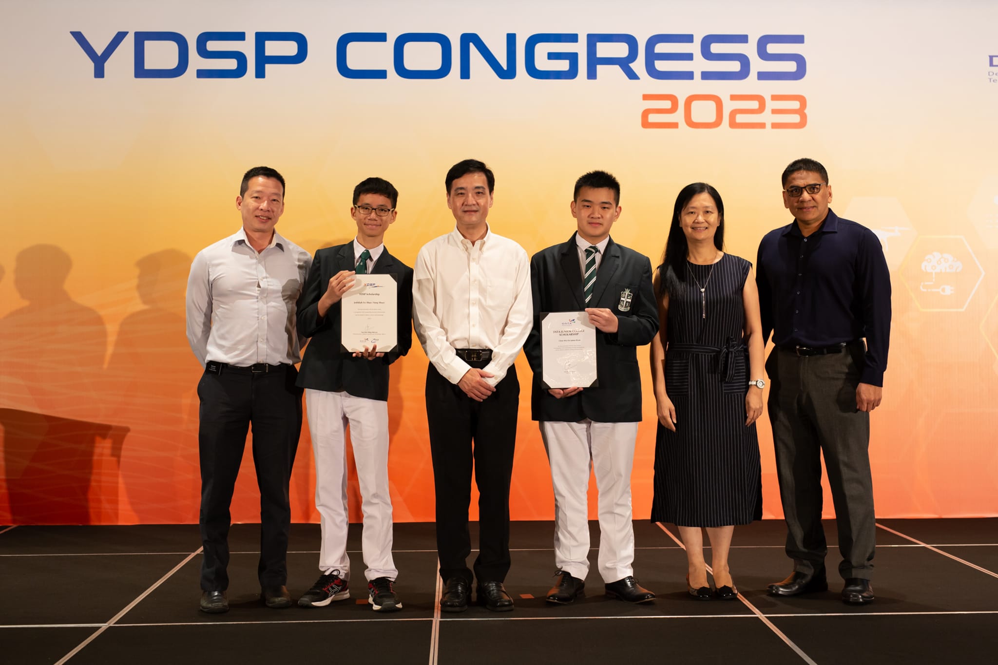 Six people posing at YDSP Congress 2023, two students in blazers holding certificates flanked by four adults.