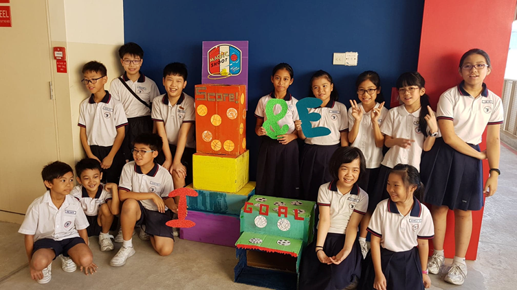 A group of school students in uniforms posing with colorful handmade stacked boxes labeled Score and Goal.