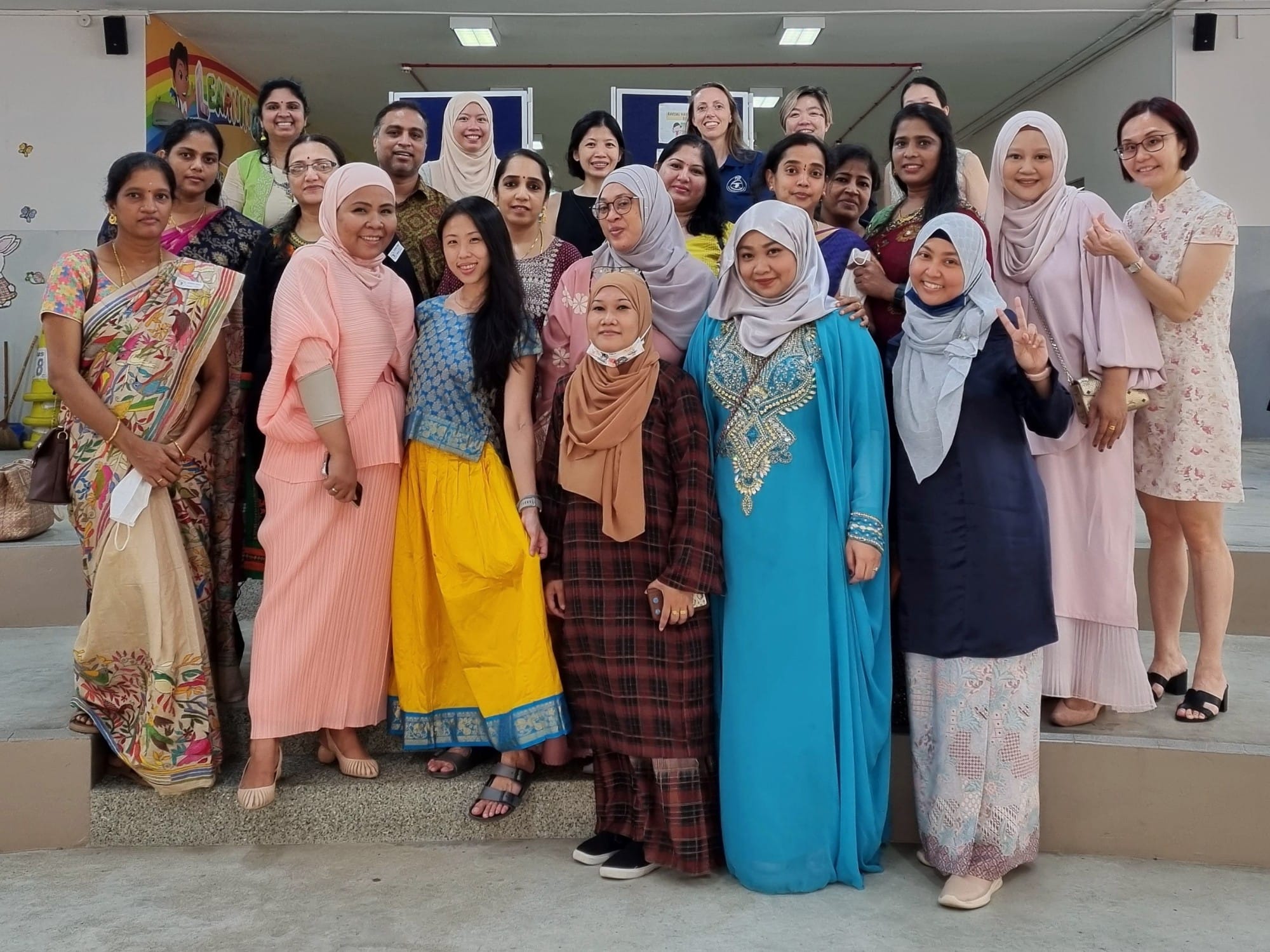 A large diverse group of women in traditional and modern attire posing together indoors, smiling at the camera.