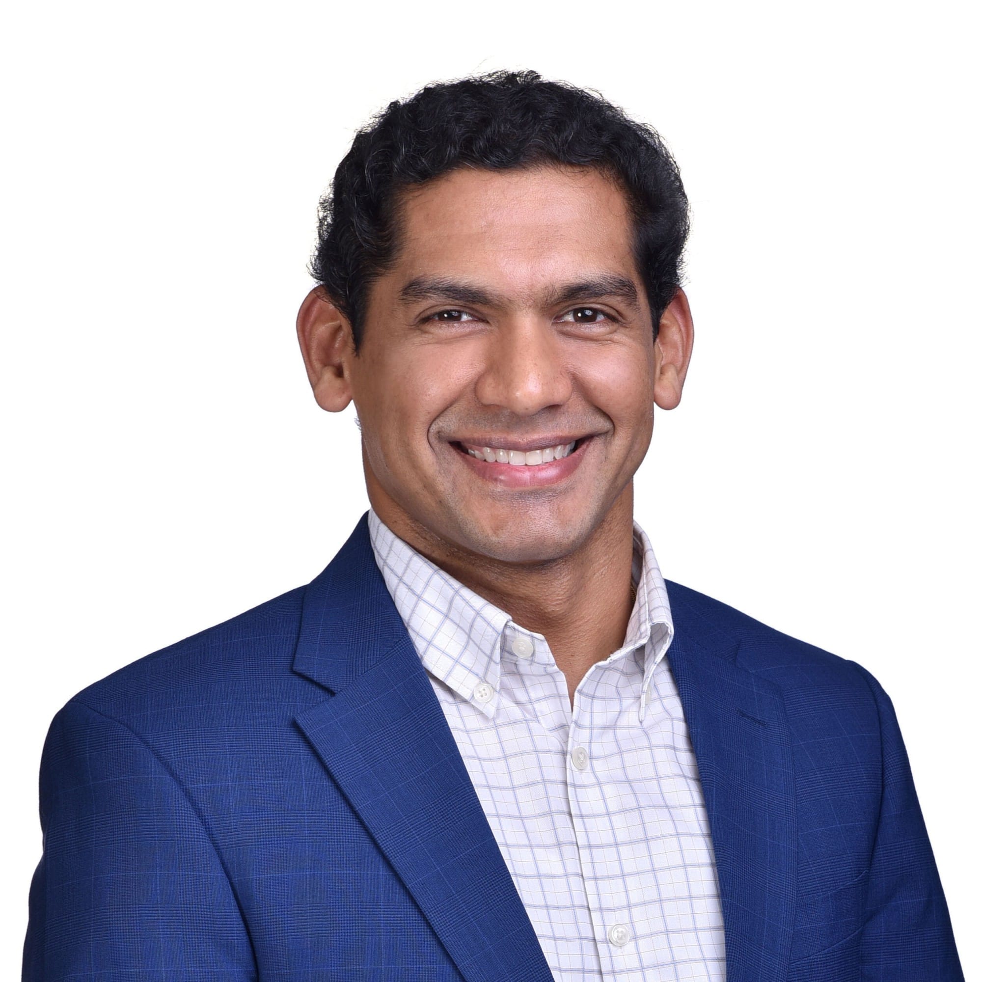 A smiling man with dark curly hair wearing a blue blazer and white checked shirt against a white background.