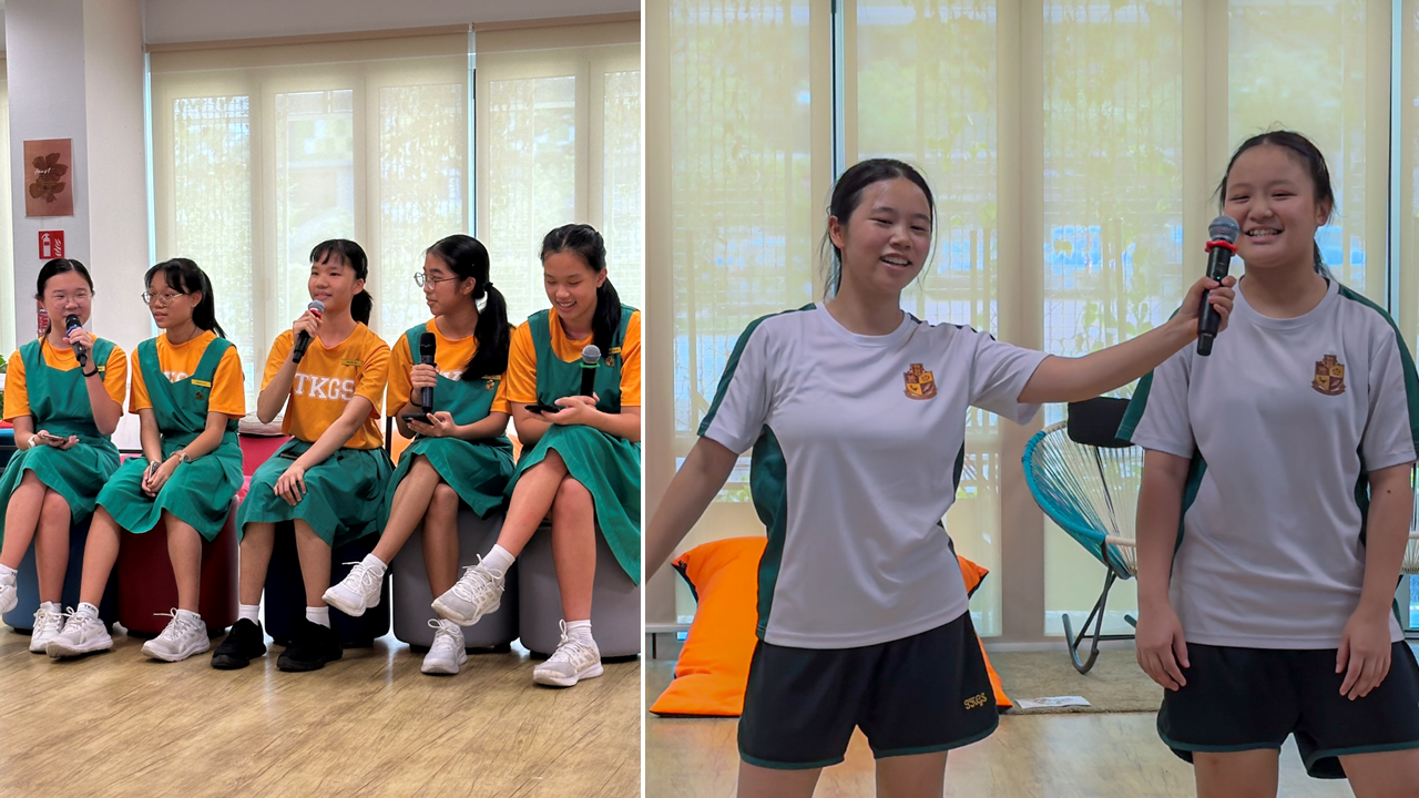 Two school girls hold a microphone while five seated schoolgirls in green and yellow uniforms speak into microphones.