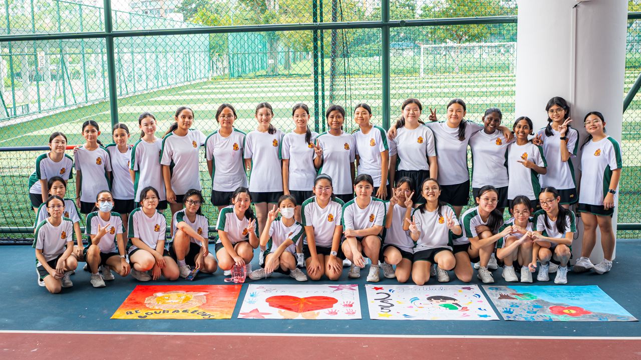 A large group of girls in matching white and green uniforms pose on a court with colorful painted posters in front.