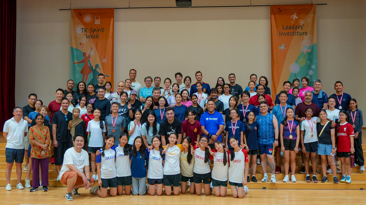 Large group of students and adults posing indoors under TK Spirit Week and Leaders Investiture banners.