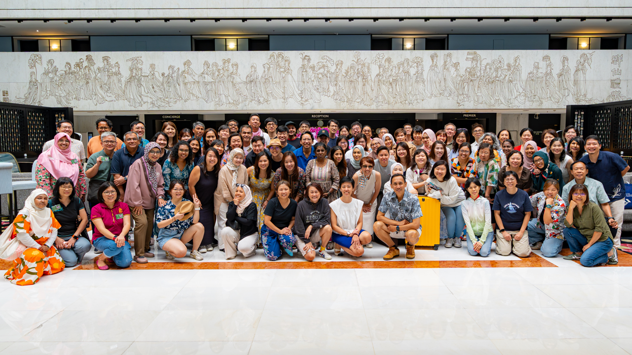 Large group of people posing together in a hotel lobby with a decorative relief mural on the wall behind them.