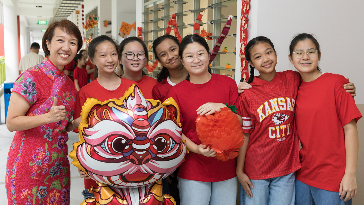 Seven smiling people in red pose with a lion dance balloon and orange decoration at a Chinese New Year celebration.