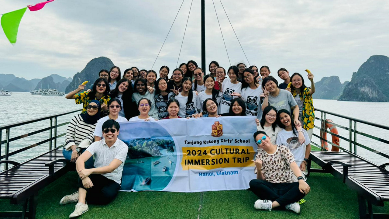 A large group of students on a boat deck holding a banner for Tanjong Katong Girls School 2024 Cultural Immersion Trip, Hanoi Vietnam.