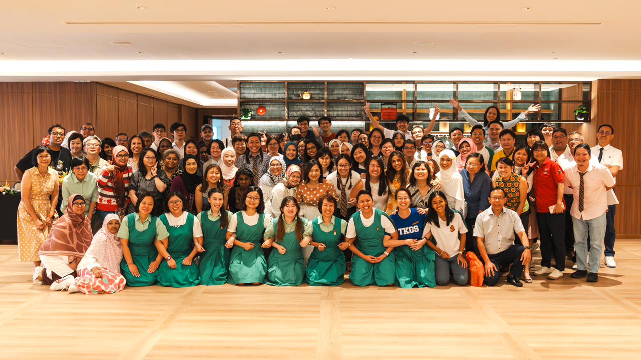 Large group of people posing together indoors, with several in the front row wearing matching green uniforms.