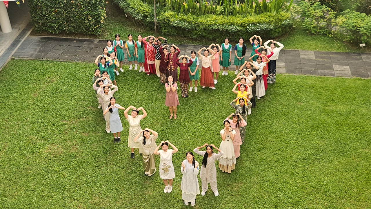 Students posing for a picture formed up in the shape of a heart on the grass patch.