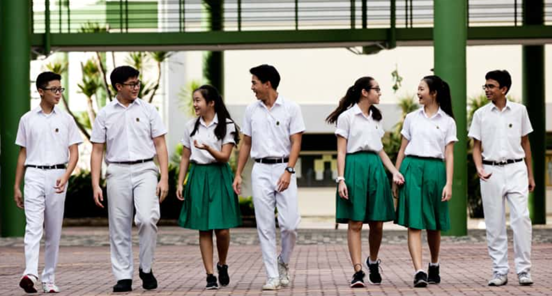 Seven students in TKSS uniform walk and chat on a school campus.
