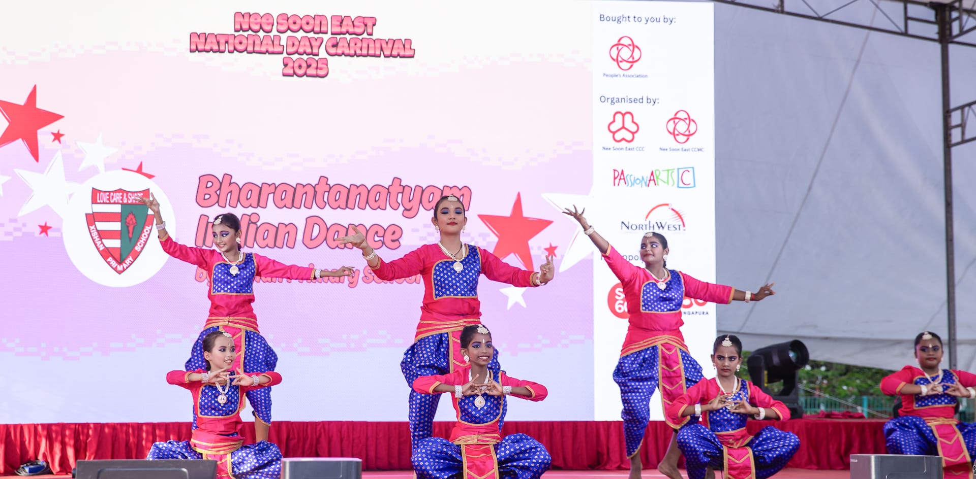 Girls in pink and blue costumes perform Bharatanatyam Indian dance on stage at Nee Soon East National Day Carnival 2025.