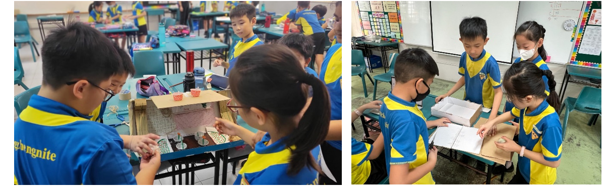Children in blue and yellow uniforms work on cardboard projects at desks in a classroom setting.