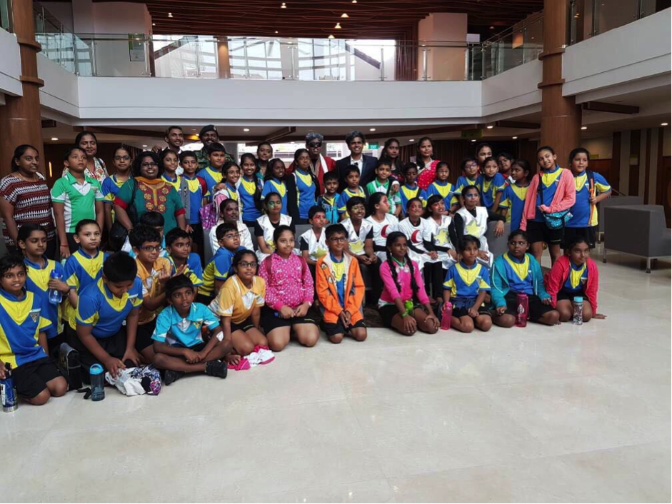 A large group of children and adults in blue and yellow sports uniforms posing together inside a modern building.