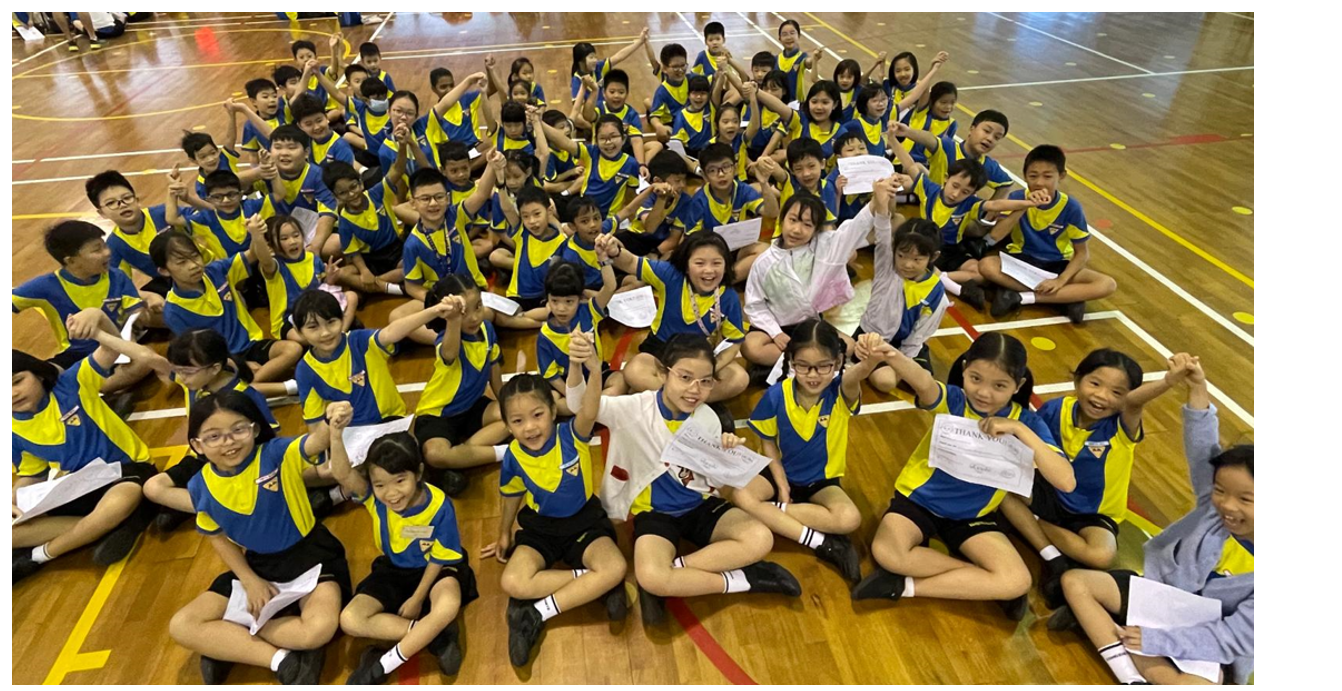 Large group of children in blue and yellow uniforms sitting and posing cheerfully on a gymnasium floor.