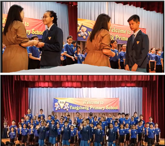 Students in blue uniforms on a stage under a Welcome to Yangzheng Primary School banner, with two receiving awards.