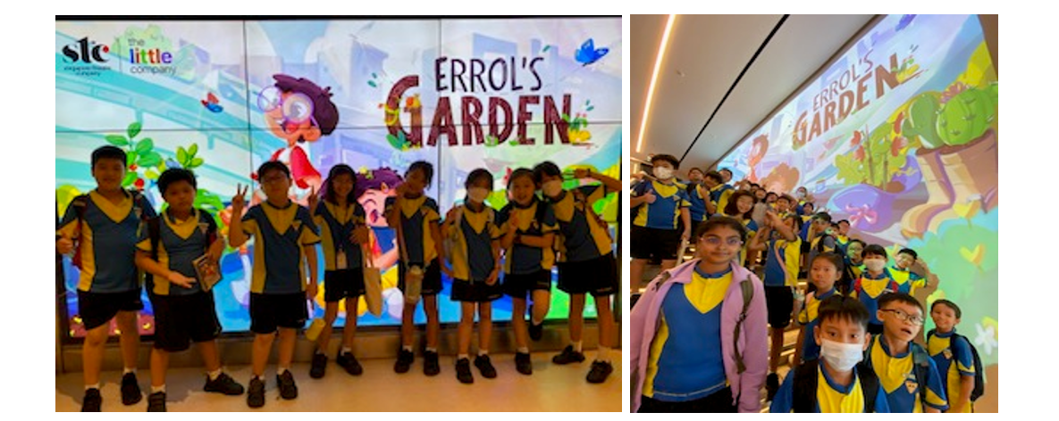 Students in blue and yellow uniforms pose in front of a colorful "Errol's Garden" display screen.
