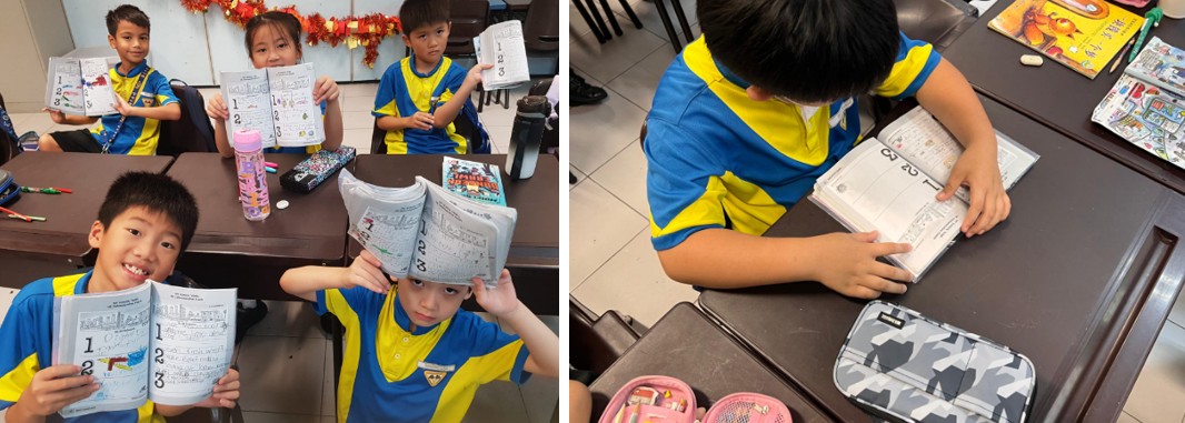Four young students in blue and yellow uniforms hold up workbooks in a classroom setting.