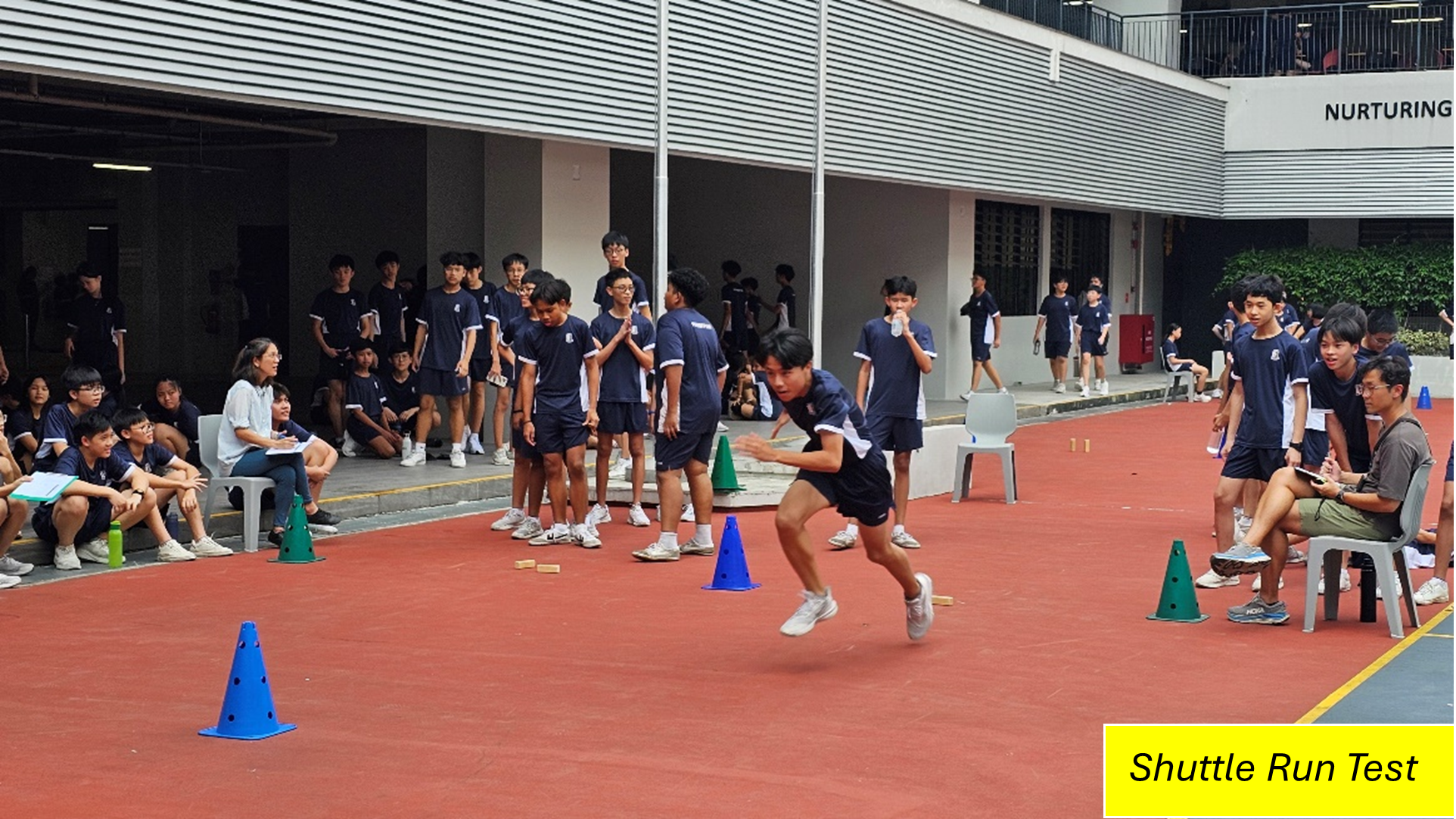 Student sprints between cones on a track as classmates and teachers watch a shuttle run test.