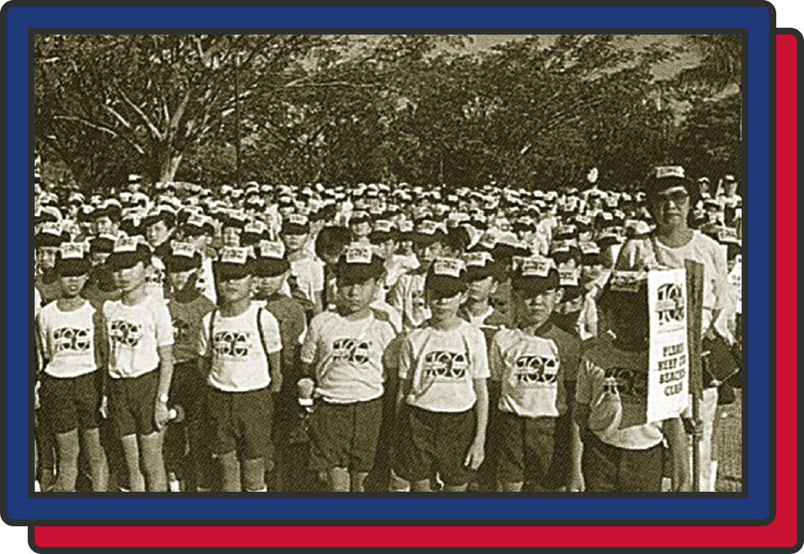Vintage sepia photo of a large group of children in matching white shirts and caps gathered outdoors.