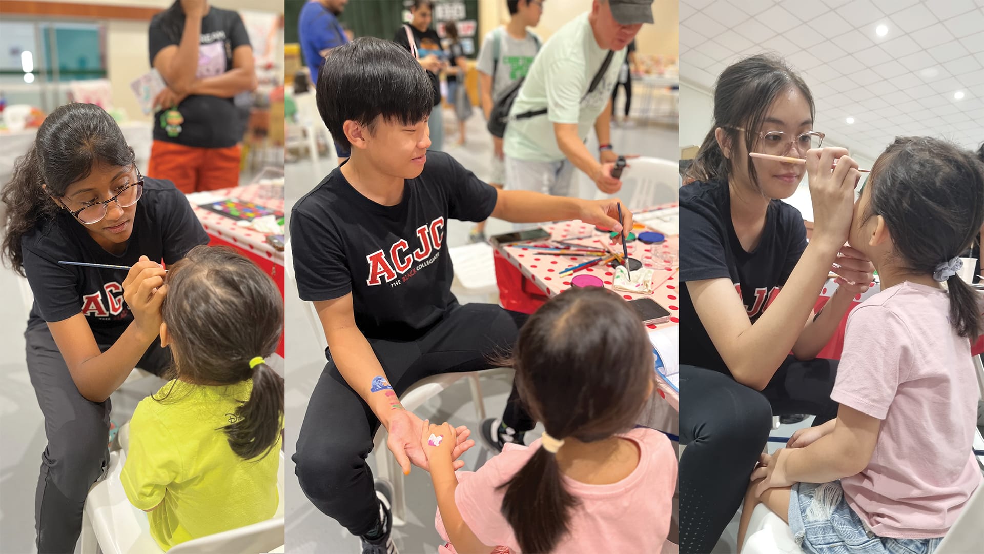 Three teens in black ACJC shirts paint faces and arms of young children at an indoor event.
