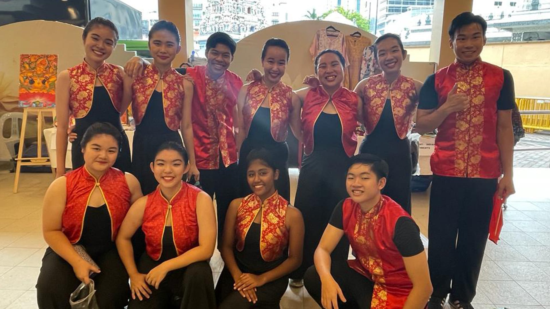 A group of eleven young people wearing matching red and gold traditional vests over black outfits, smiling together indoors.