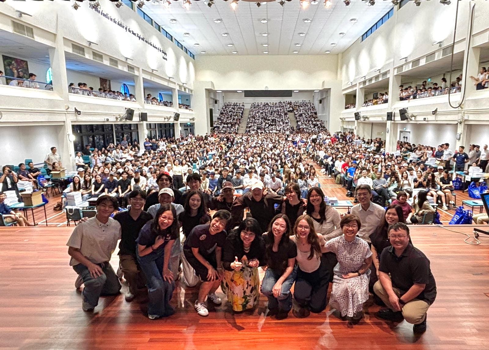 Large group of people posing on a stage in a packed auditorium filled with hundreds of attendees on multiple levels.