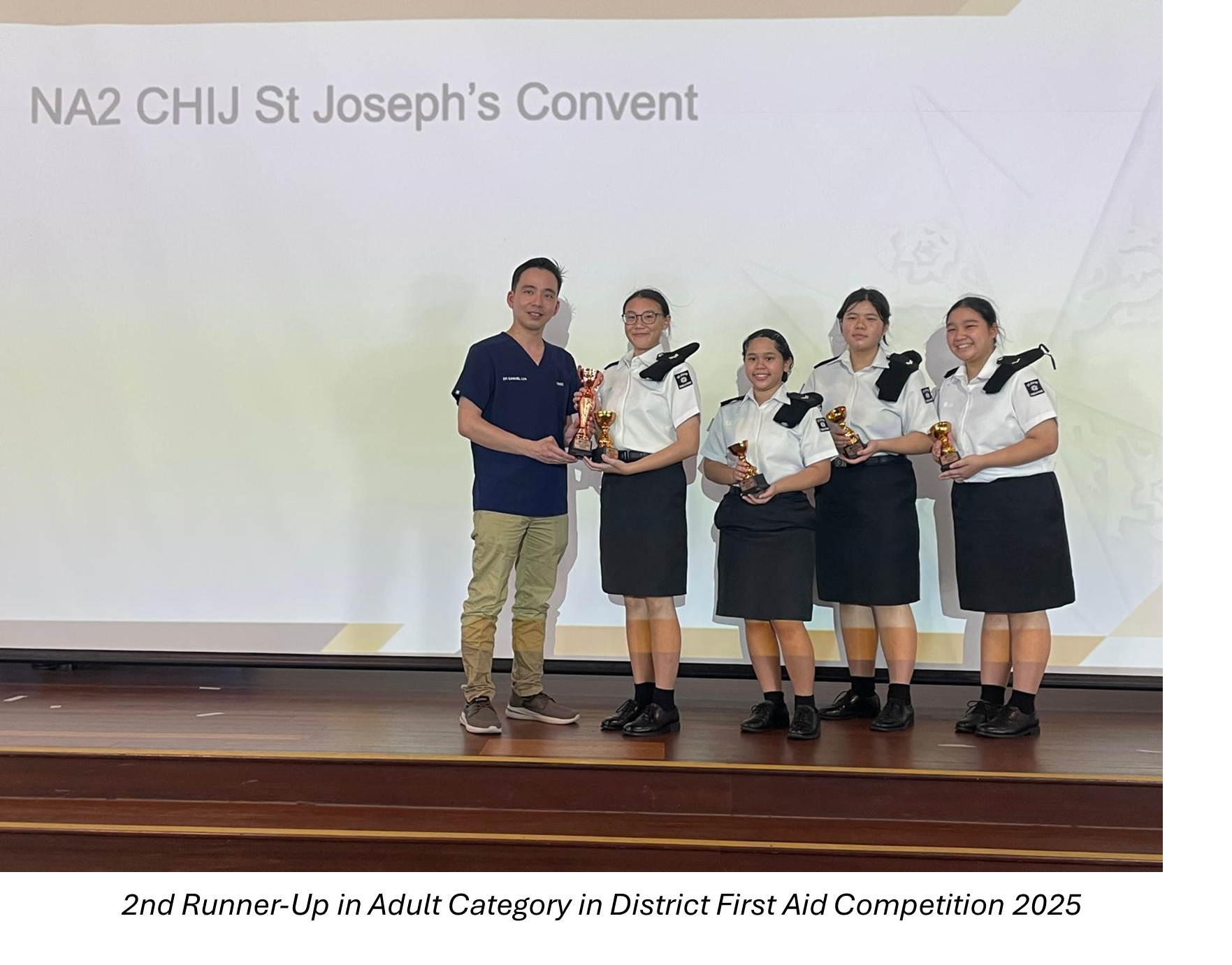 Five people on a stage hold trophies, with a slide reading NA2 CHIJ St Joseph's Convent behind them.