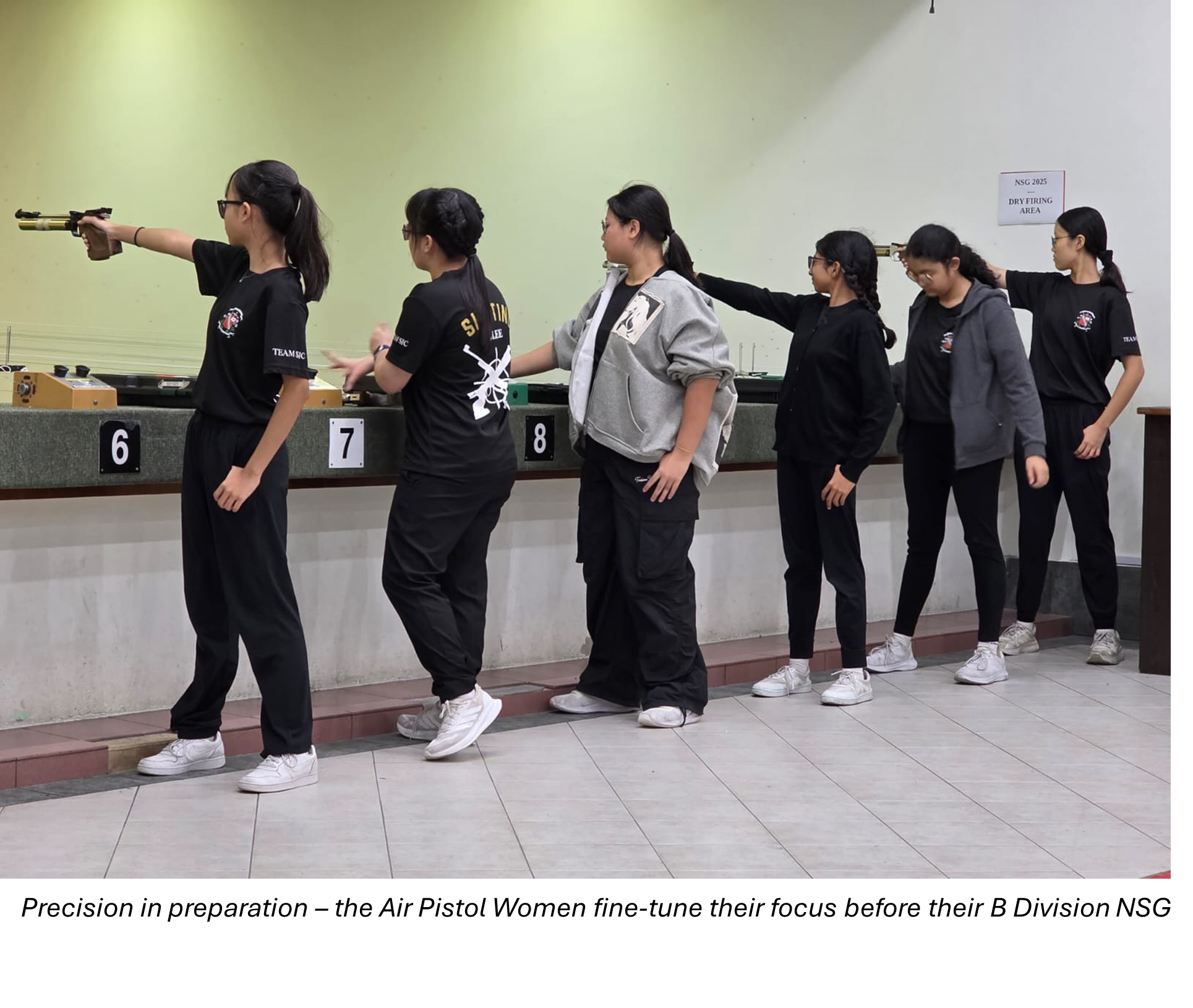 Six young women at a shooting range, one aiming an air pistol at lane 6 while others stand watching nearby.