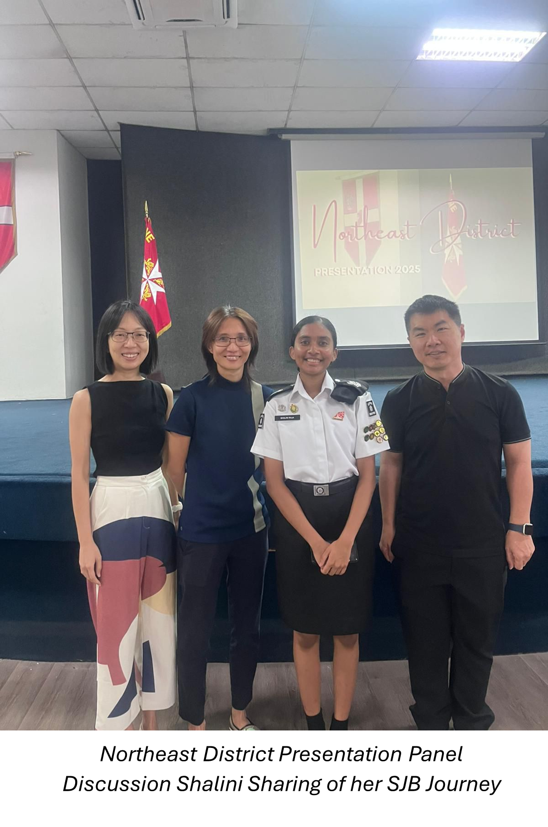 Four people smiling indoors at Northeast District Presentation 2025, one wearing a white SJB uniform with badges.