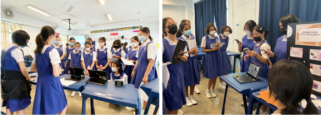 Students in blue uniforms and masks gather around desks with laptops during a classroom presentation event.