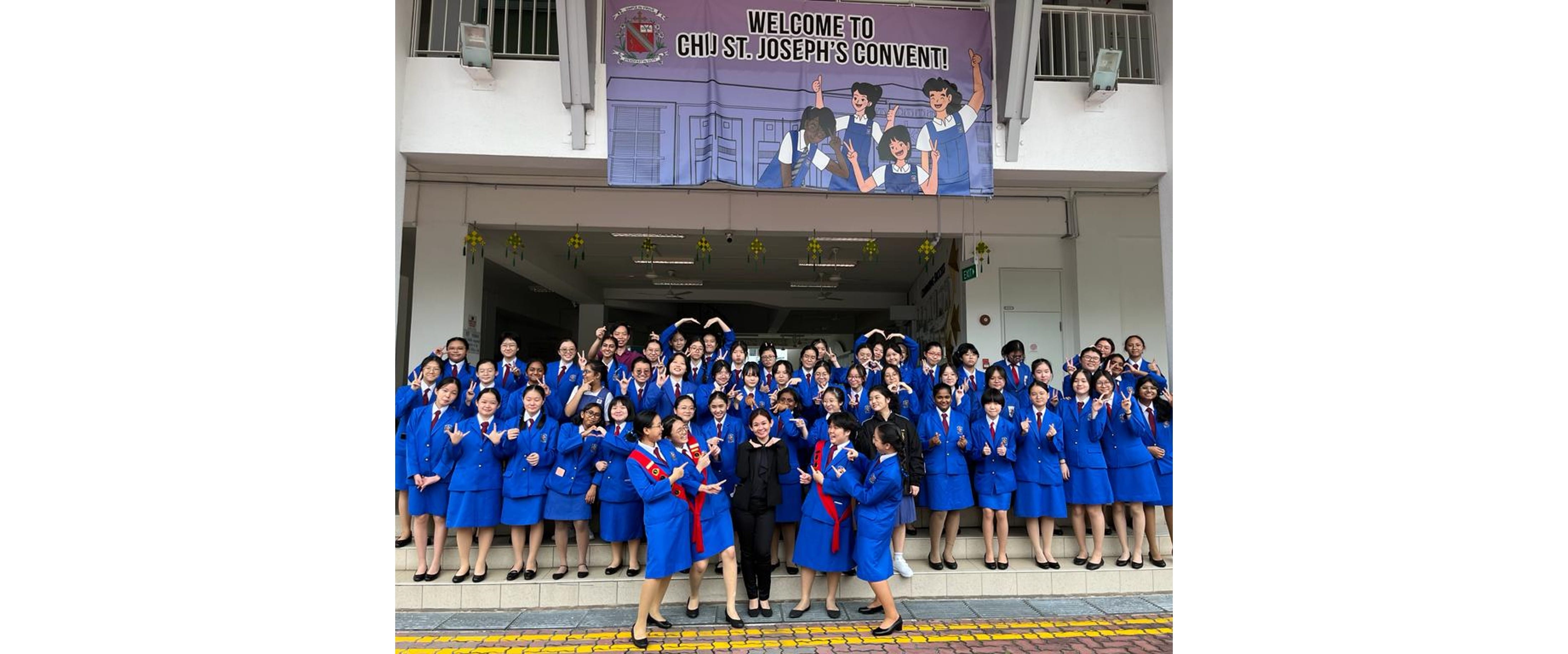 Large group of students in blue uniforms posing outside CHIJ St. Joseph's Convent under a welcome banner.