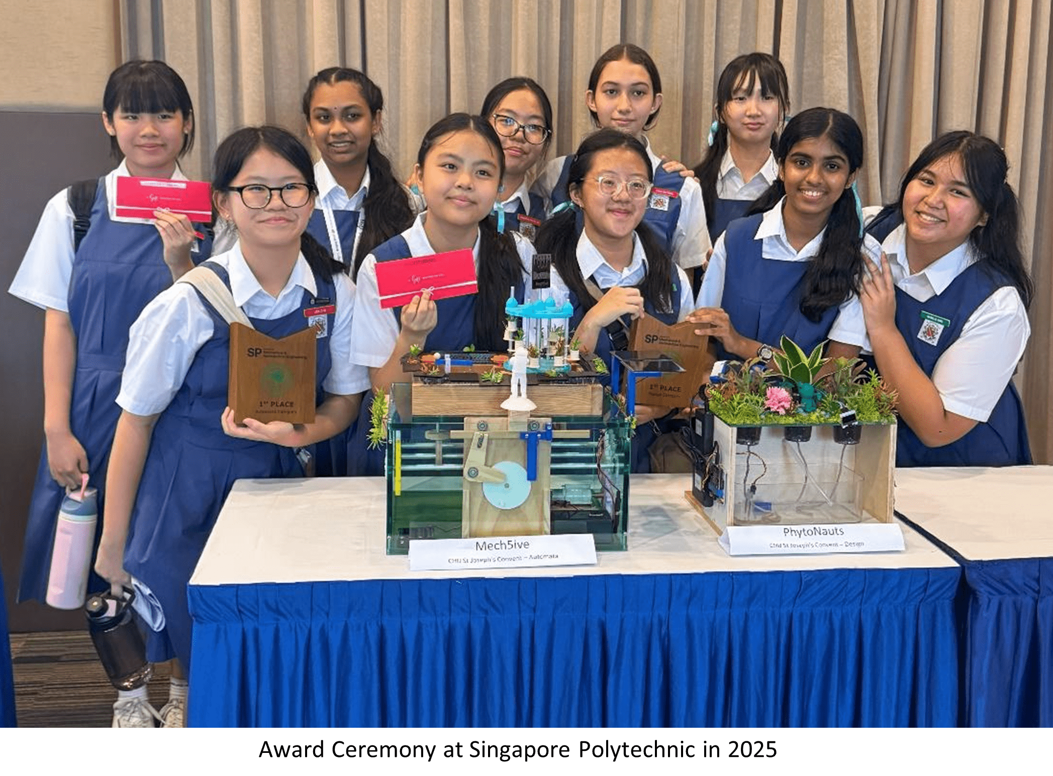 Ten schoolgirls in blue uniforms hold first place awards beside project models at a 2025 Singapore Polytechnic ceremony.