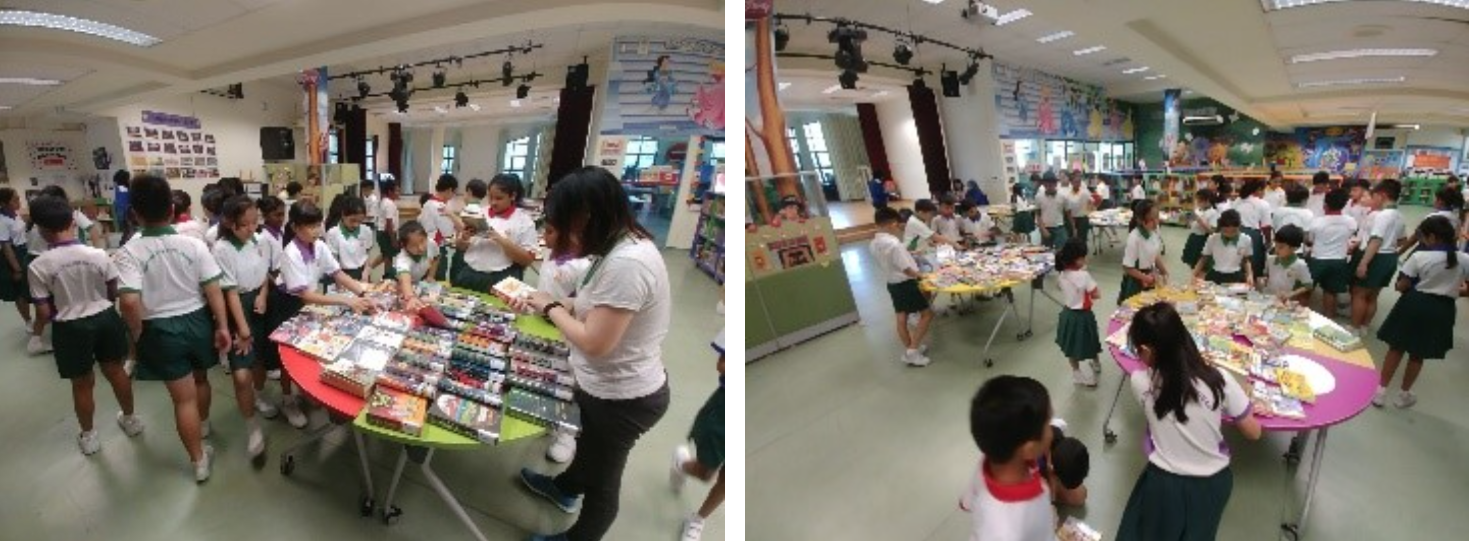 Students in school uniforms browse books and materials on tables in a colorful school library or hall.