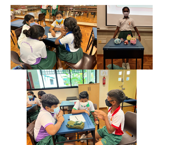 Students in uniforms and masks work in groups at desks, while one student presents items on a table.
